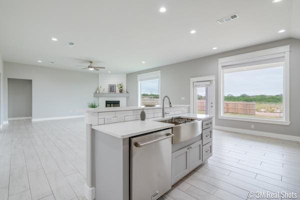 kitchen with sink, light wood-type flooring, stainless steel dishwasher, an island with sink, and a fireplace