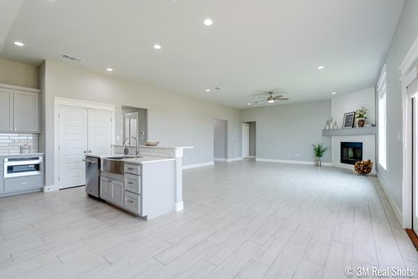 kitchen featuring sink, a kitchen island with sink, stainless steel appliances, a fireplace, and decorative backsplash