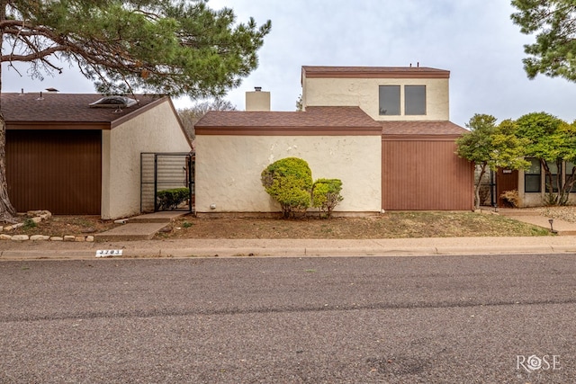 view of home's exterior featuring stucco siding, a shingled roof, a chimney, and a gate