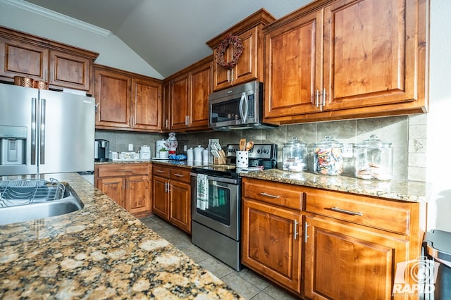 kitchen featuring tasteful backsplash, light stone counters, vaulted ceiling, light tile patterned floors, and stainless steel appliances