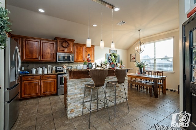 kitchen with appliances with stainless steel finishes, backsplash, hanging light fixtures, a kitchen bar, and dark stone counters