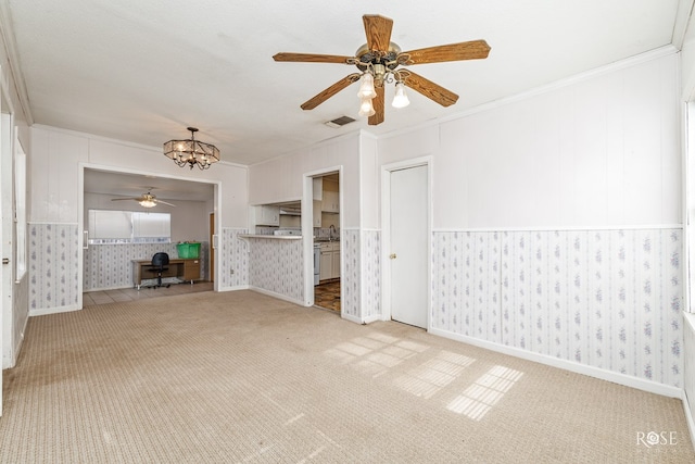 unfurnished living room with crown molding, ceiling fan with notable chandelier, and light colored carpet