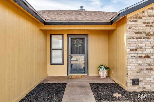 doorway to property featuring a patio and roof with shingles