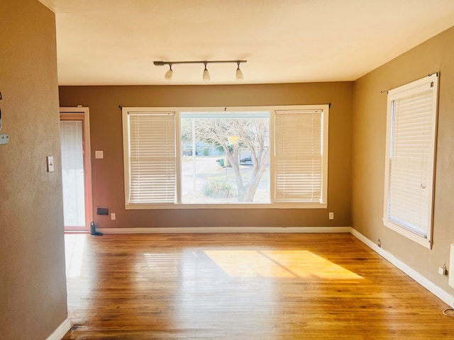 unfurnished room with wood finished floors, rail lighting, and baseboards