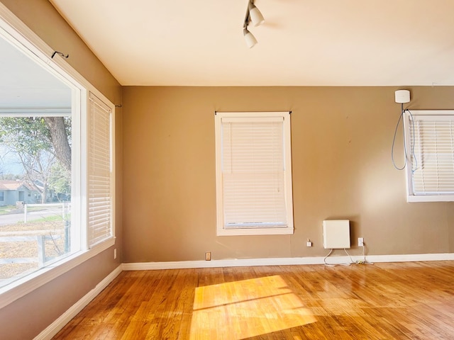 empty room featuring wood finished floors, rail lighting, and baseboards