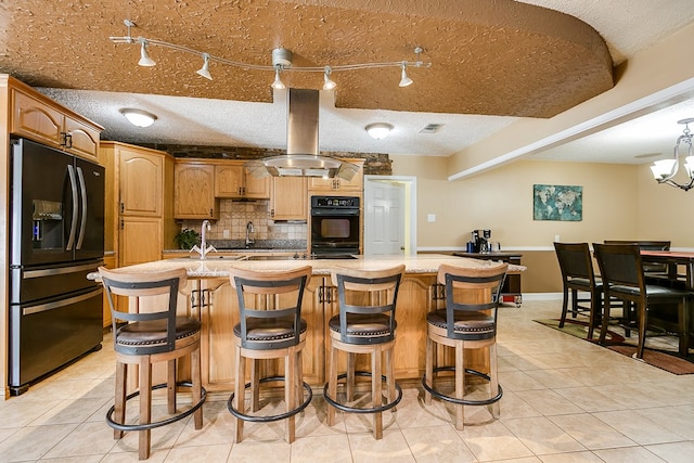 kitchen featuring a kitchen island with sink, light tile patterned floors, island range hood, and black appliances