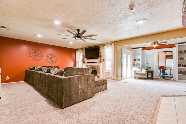 living room featuring a textured ceiling, a fireplace, light colored carpet, and ceiling fan