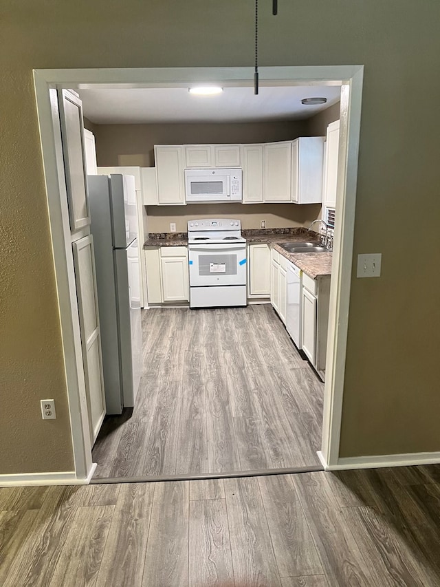 kitchen with white cabinetry, sink, white appliances, and hardwood / wood-style floors