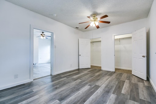 unfurnished bedroom with a textured ceiling, visible vents, wood finished floors, baseboards, and multiple closets