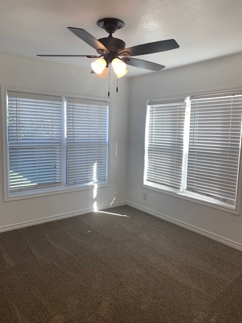 empty room featuring ceiling fan and dark colored carpet