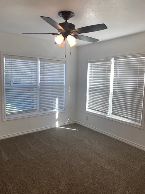 spare room with ceiling fan and dark colored carpet