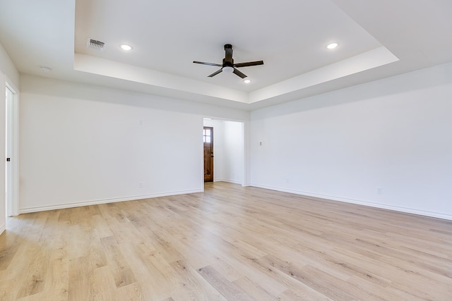 unfurnished room with a raised ceiling, ceiling fan, and light hardwood / wood-style flooring