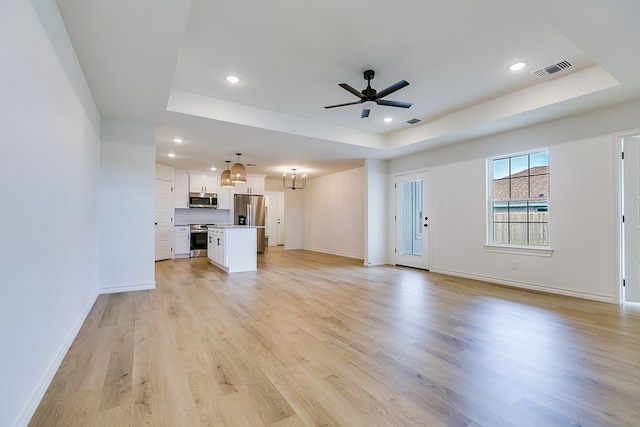 unfurnished living room with a tray ceiling, ceiling fan, and light wood-type flooring