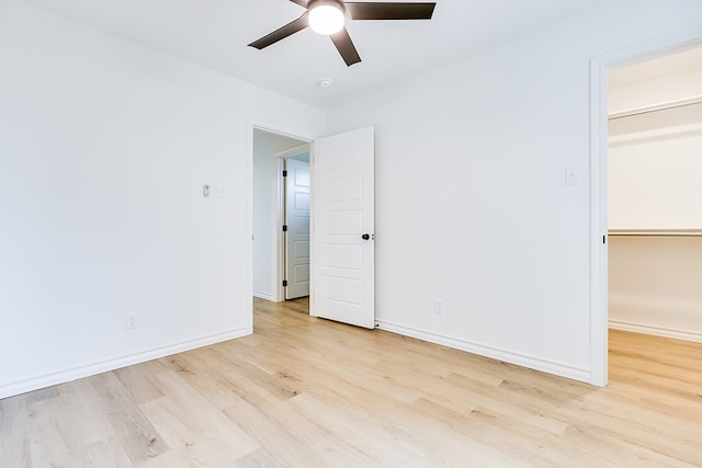 unfurnished bedroom featuring ceiling fan, a spacious closet, a closet, and light wood-type flooring