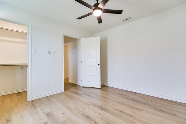 unfurnished bedroom featuring a spacious closet, a closet, ceiling fan, and light wood-type flooring