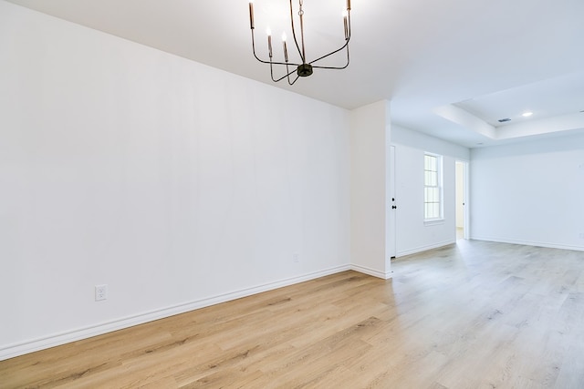 interior space featuring an inviting chandelier, a tray ceiling, and light wood-type flooring