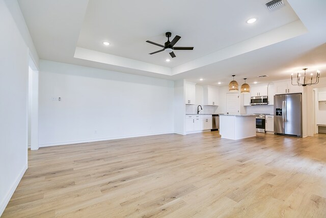 unfurnished living room featuring sink, light hardwood / wood-style flooring, ceiling fan, and a tray ceiling