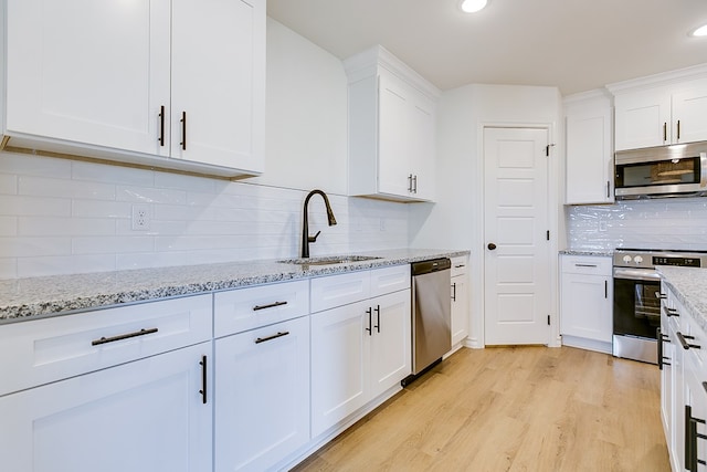 kitchen with sink, white cabinetry, light wood-type flooring, stainless steel appliances, and backsplash