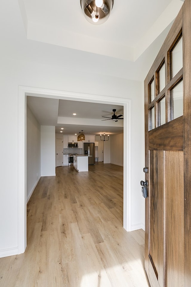 entrance foyer featuring ceiling fan, a raised ceiling, and light hardwood / wood-style flooring