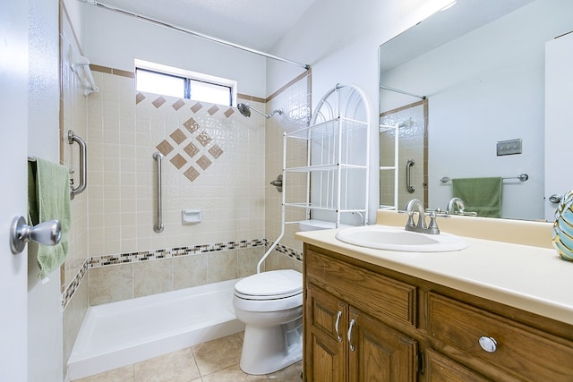 bathroom featuring tile patterned flooring, toilet, vanity, and a tile shower