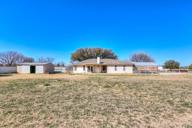 back of property with an outbuilding, a lawn, and fence