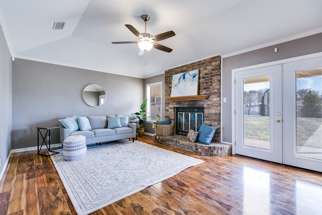 living area with wood finished floors, visible vents, ornamental molding, vaulted ceiling, and a brick fireplace