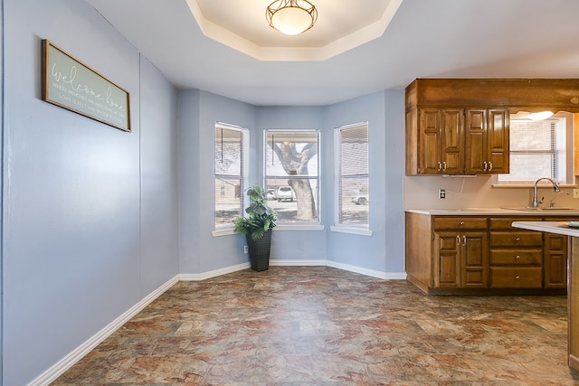 kitchen featuring baseboards, a sink, light countertops, a raised ceiling, and brown cabinets