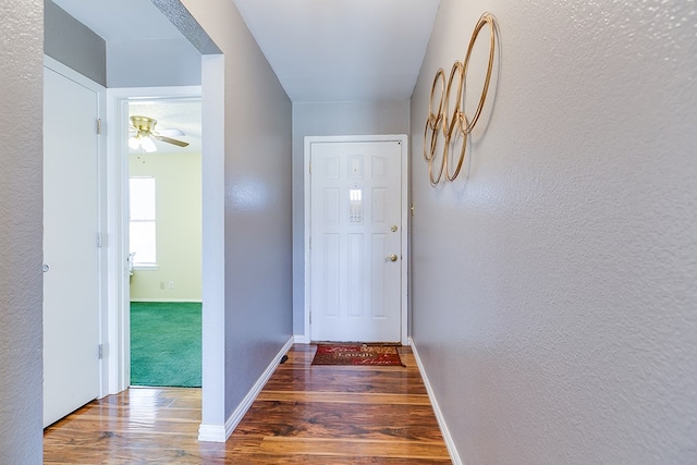 corridor with wood finished floors, baseboards, and a textured wall