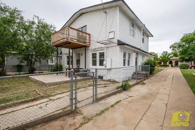 view of front facade with a balcony, brick siding, fence, and a gate