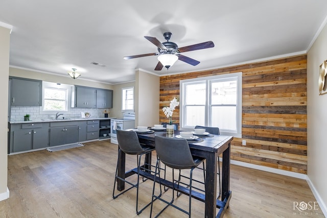 34 W 9th St, San Angelo, TX 76903 - dining space with ornamental molding, wooden walls, light wood-style flooring, a ceiling fan, and baseboards