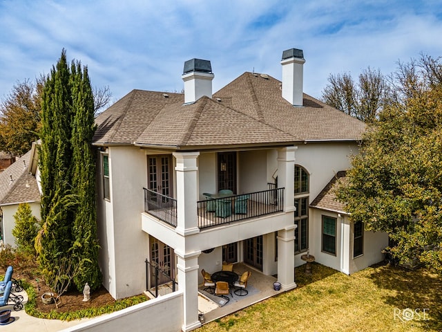 rear view of house featuring roof with shingles, stucco siding, a chimney, a yard, and a patio area