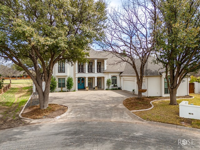 view of front facade with a shingled roof, concrete driveway, stucco siding, a garage, and a balcony