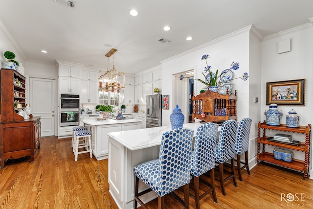 kitchen featuring visible vents, light countertops, white cabinets, appliances with stainless steel finishes, and a kitchen breakfast bar