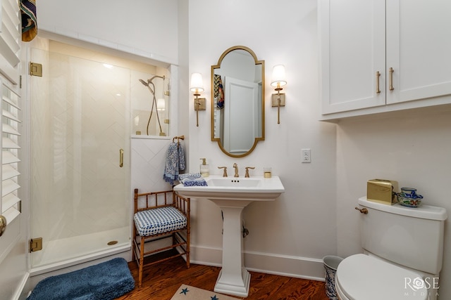 bathroom with a shower stall, toilet, baseboards, and wood finished floors