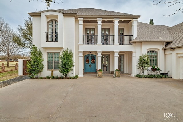 view of front of home with a balcony, french doors, roof with shingles, and stucco siding