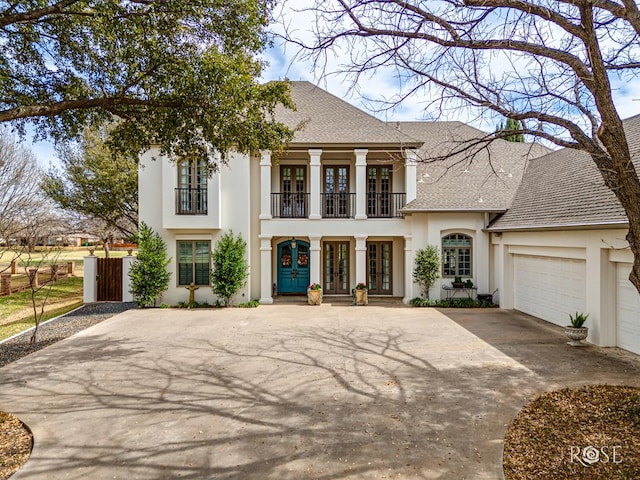 greek revival house featuring concrete driveway, roof with shingles, stucco siding, french doors, and a balcony