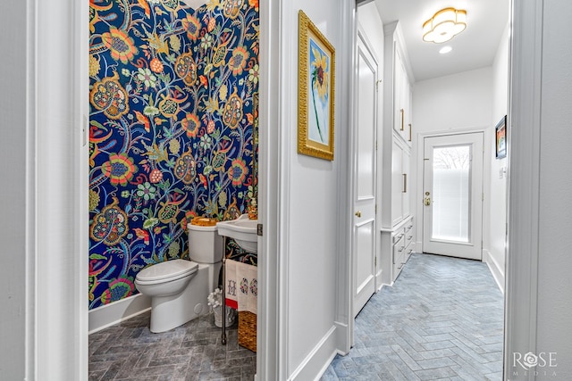 half bath with brick floor, baseboards, and toilet