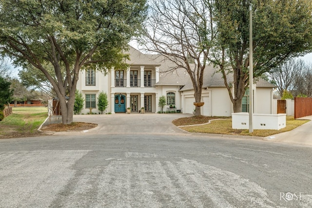 view of front of home with a balcony, fence, driveway, an attached garage, and stucco siding