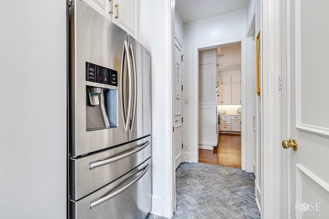 kitchen featuring stainless steel fridge, white cabinets, and brick floor