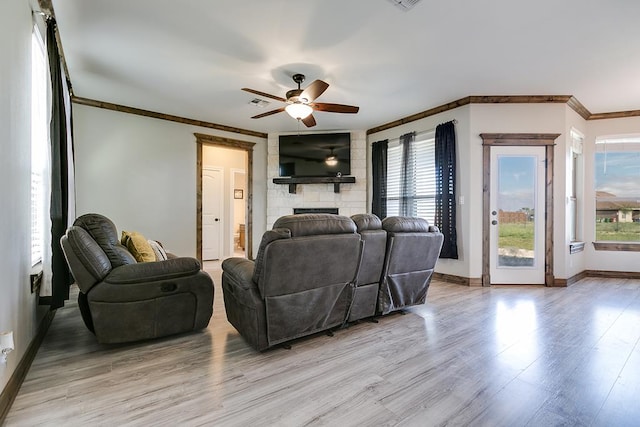 living room with ceiling fan, plenty of natural light, a stone fireplace, and light hardwood / wood-style flooring