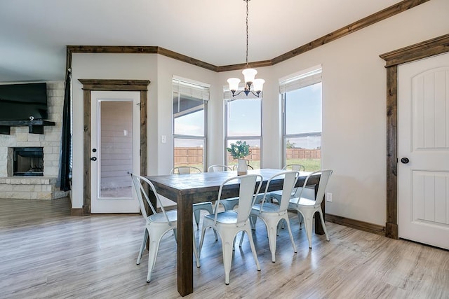 dining space featuring a notable chandelier, ornamental molding, a fireplace, and light wood-type flooring