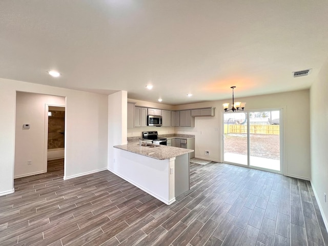 kitchen with gray cabinets, appliances with stainless steel finishes, a peninsula, a chandelier, and wood tiled floor