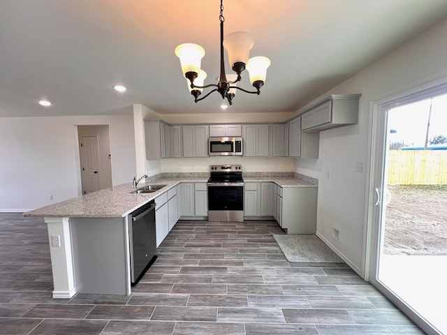 kitchen with a sink, a peninsula, appliances with stainless steel finishes, and gray cabinetry