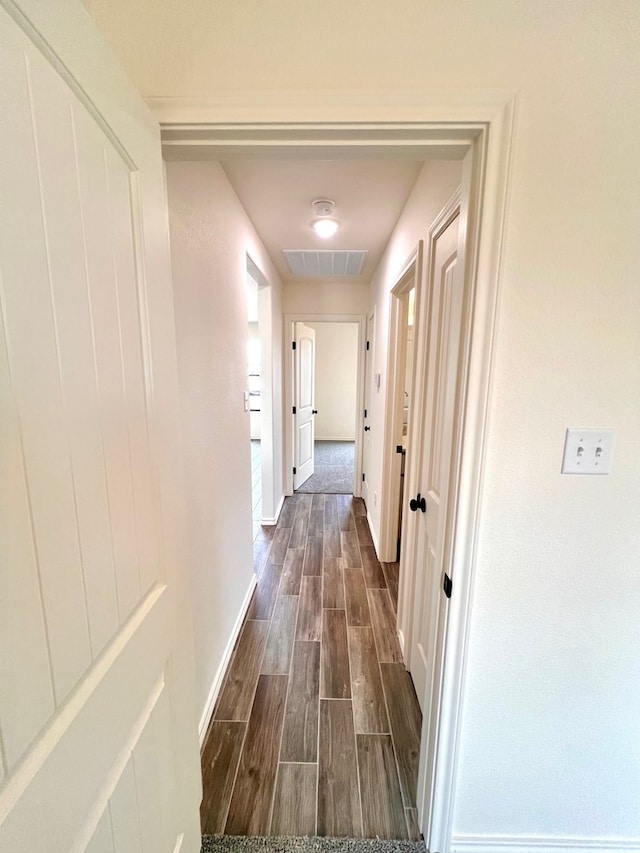 hallway featuring baseboards, visible vents, and wood finish floors