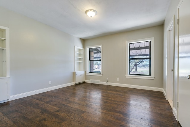 empty room with dark hardwood / wood-style floors and built in features