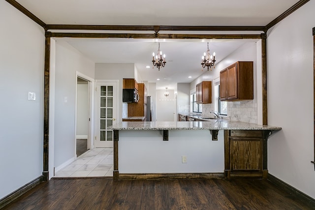 kitchen featuring hardwood / wood-style flooring, stainless steel appliances, light stone counters, kitchen peninsula, and a chandelier