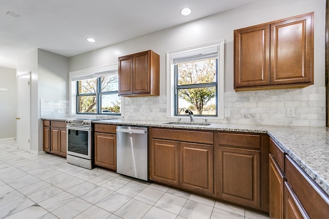 kitchen with light stone counters, sink, decorative backsplash, and stainless steel appliances