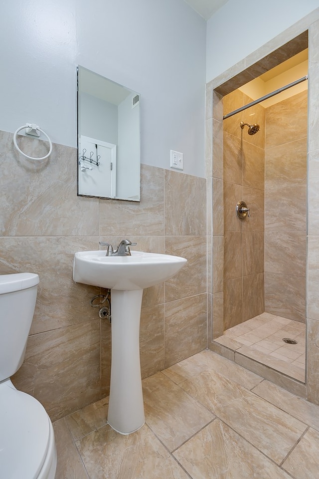 bathroom featuring a tile shower, tile walls, and toilet