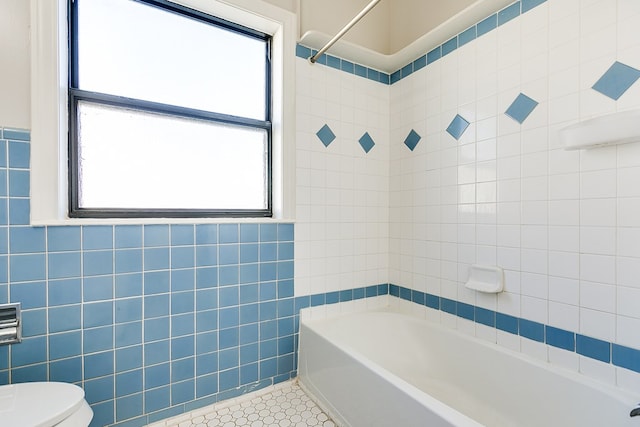 bathroom featuring shower / washtub combination, toilet, tile patterned flooring, and tile walls