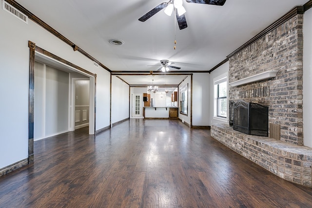 unfurnished living room with crown molding, a brick fireplace, dark wood-type flooring, and ceiling fan with notable chandelier